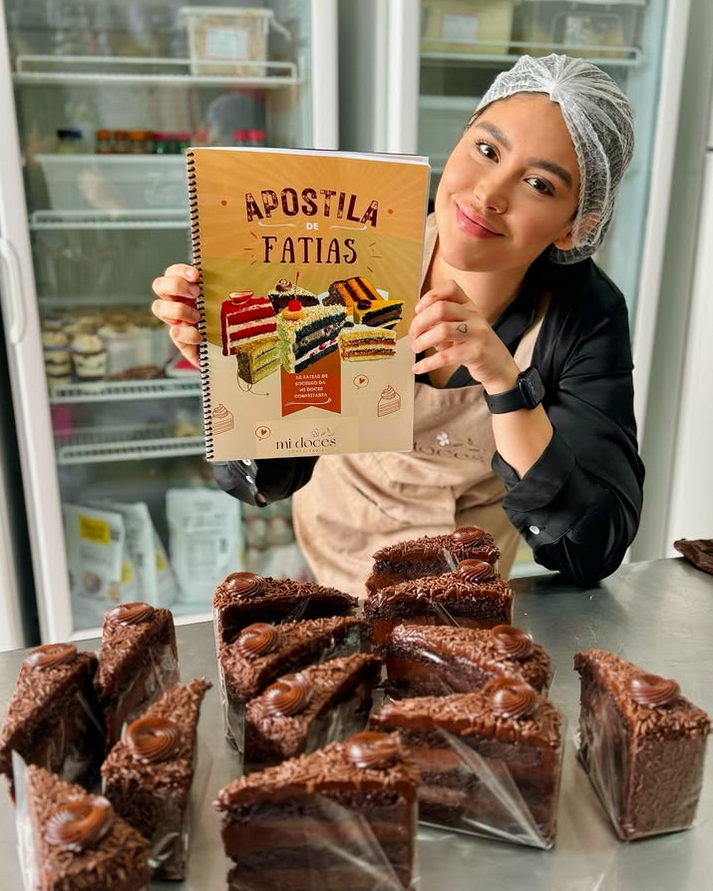 Millena Moreira segurando a Apostila de Fatias com bolos ao fundo